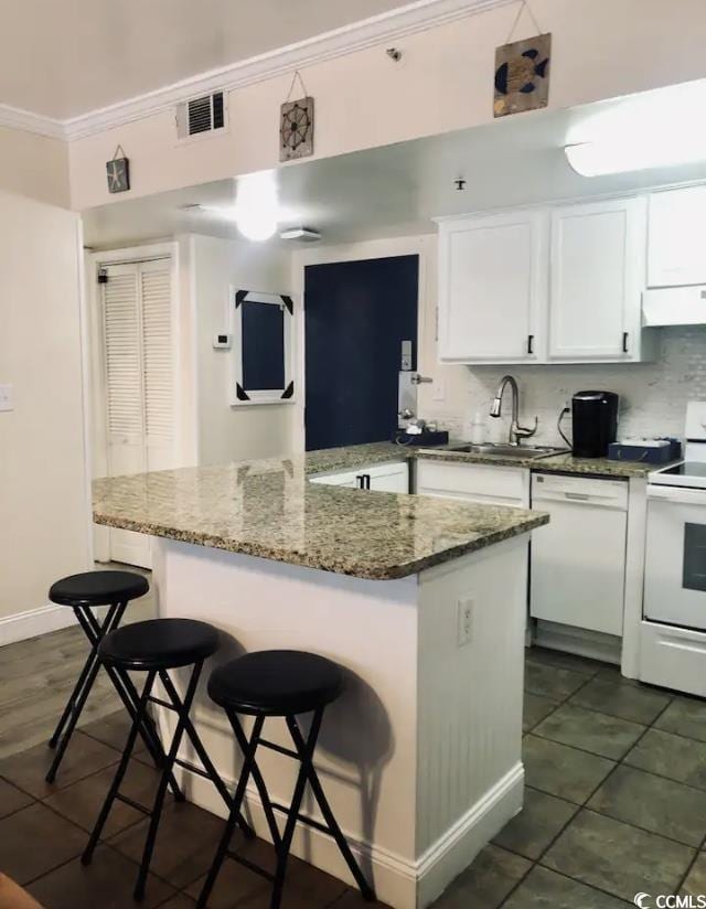 kitchen with sink, dark stone countertops, a kitchen breakfast bar, white appliances, and white cabinets