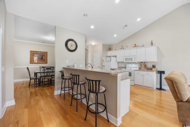 kitchen with a kitchen bar, white cabinets, kitchen peninsula, light wood-type flooring, and white appliances