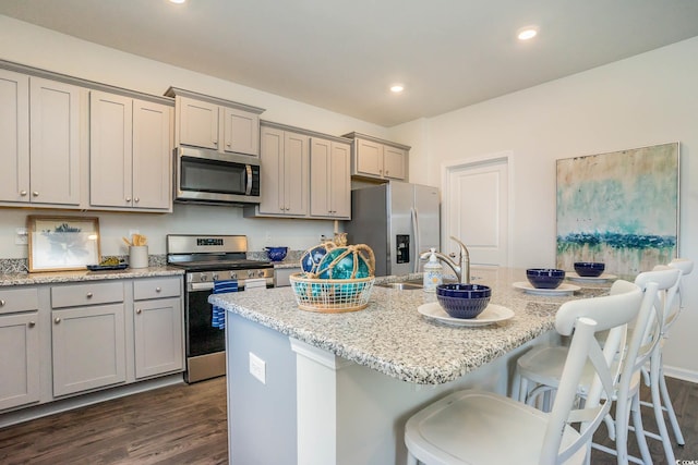 kitchen with light stone counters, stainless steel appliances, a kitchen island with sink, and dark wood-type flooring