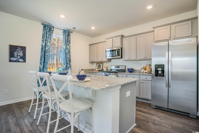 kitchen featuring light stone countertops, stainless steel appliances, dark hardwood / wood-style flooring, gray cabinets, and a center island with sink