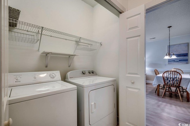 clothes washing area featuring hardwood / wood-style floors, washer and clothes dryer, a textured ceiling, and an inviting chandelier