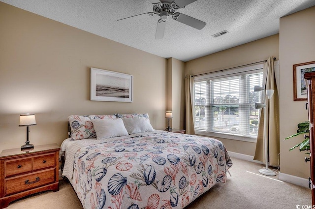 bedroom with ceiling fan, light colored carpet, and a textured ceiling