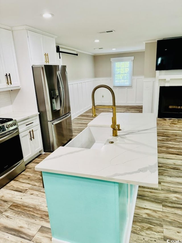 3936 Murrells Inlet Rd, Murrells Inlet, SC 29576 - kitchen with appliances with stainless steel finishes, white cabinetry, light stone counters, a wainscoted wall, and crown molding
