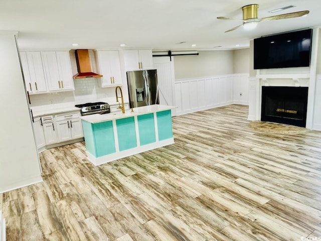 3936 Murrells Inlet Rd, Murrells Inlet, SC 29576 - kitchen with appliances with stainless steel finishes, wall chimney range hood, light wood-style flooring, a barn door, and a ceiling fan