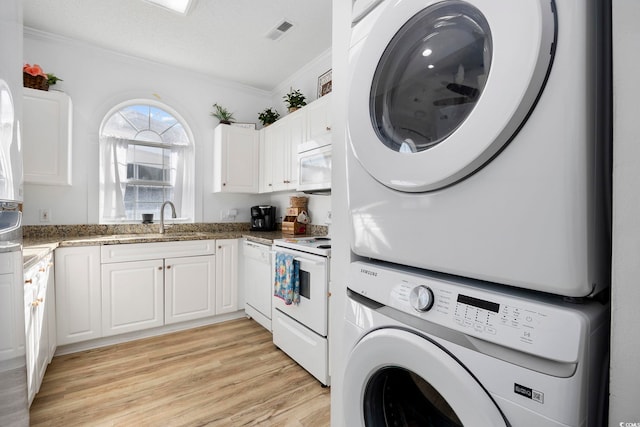 laundry room with light wood-type flooring, visible vents, stacked washer and dryer, ornamental molding, and a sink