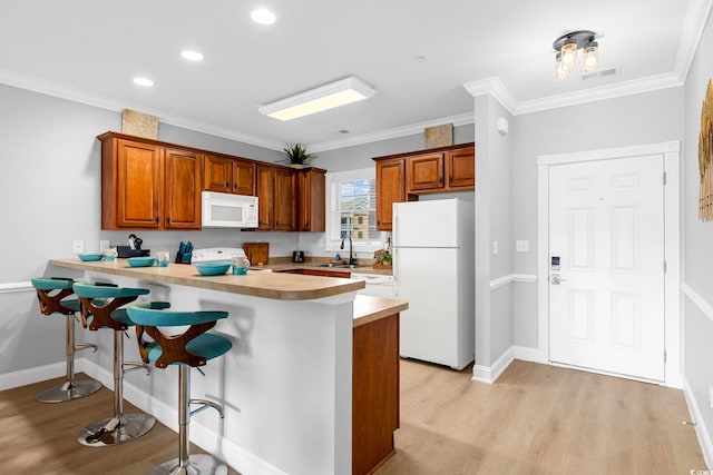 kitchen featuring a kitchen breakfast bar, kitchen peninsula, crown molding, and white appliances