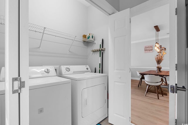 clothes washing area featuring crown molding, washer and dryer, and light wood-type flooring