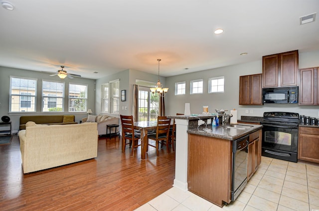 kitchen with a kitchen island with sink, light wood-type flooring, black appliances, ceiling fan with notable chandelier, and pendant lighting