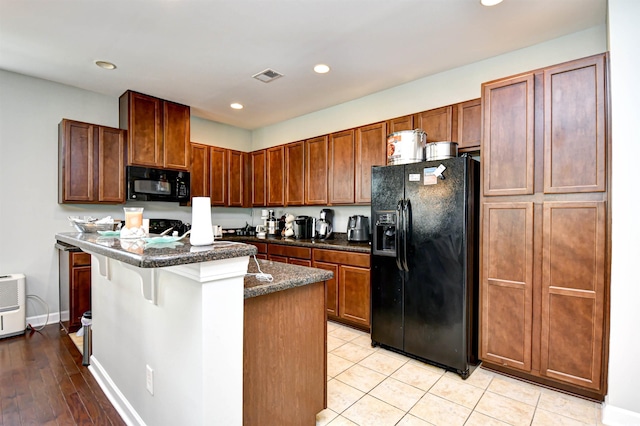 kitchen featuring black appliances, a center island, a kitchen bar, and light hardwood / wood-style floors