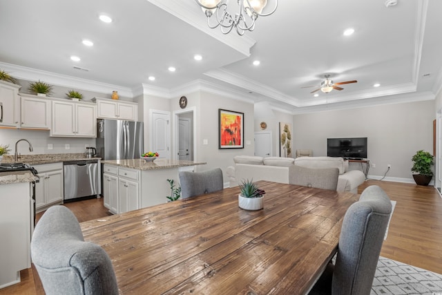 dining area featuring ceiling fan with notable chandelier, sink, crown molding, a raised ceiling, and light hardwood / wood-style floors