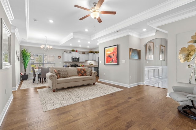 living room with a tray ceiling, crown molding, ceiling fan with notable chandelier, and light hardwood / wood-style floors