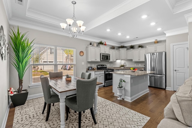 dining space featuring dark wood-type flooring, a notable chandelier, ornamental molding, and sink