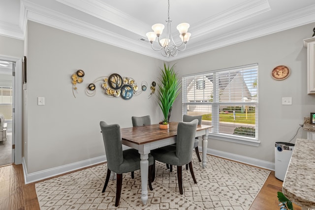 dining area featuring a notable chandelier, ornamental molding, a tray ceiling, and light wood-type flooring