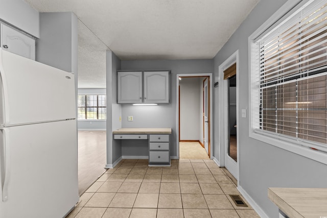 kitchen with built in desk, a textured ceiling, white refrigerator, and gray cabinets