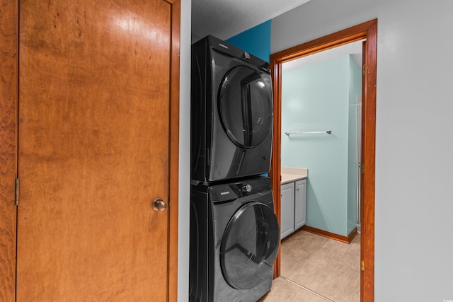 clothes washing area with cabinets, stacked washer and dryer, and light tile patterned floors