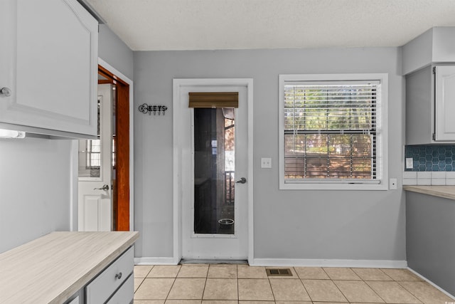 kitchen featuring white cabinetry, tasteful backsplash, light tile patterned flooring, and a textured ceiling