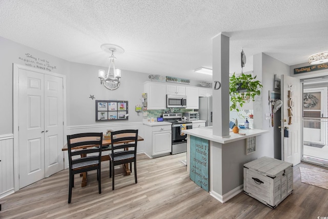 kitchen featuring white cabinetry, decorative light fixtures, stainless steel appliances, and light wood-type flooring