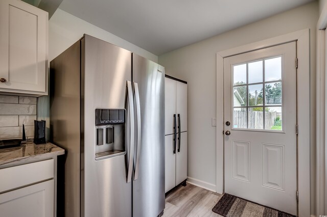 kitchen with stainless steel fridge with ice dispenser, white cabinetry, light wood-type flooring, light stone countertops, and backsplash
