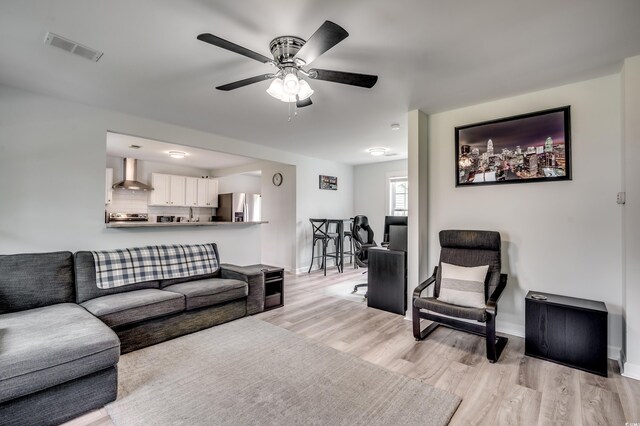 living room featuring light wood-type flooring, ceiling fan, baseboards, and visible vents