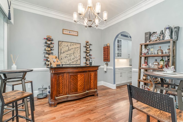 dining room featuring a dry bar, light wood-style floors, a notable chandelier, and crown molding