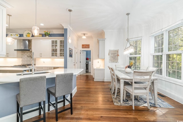 kitchen with tasteful backsplash, dark wood-style flooring, light countertops, wall chimney range hood, and pendant lighting