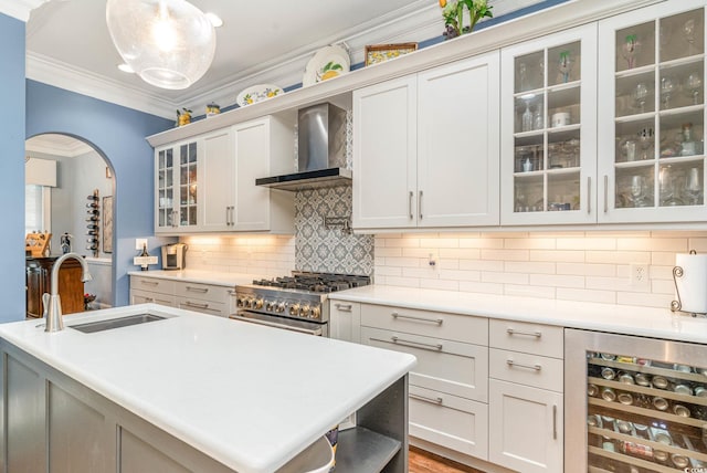 kitchen with beverage cooler, wall chimney exhaust hood, ornamental molding, high end stainless steel range, and a sink