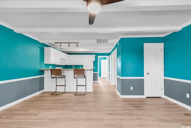 kitchen with white cabinets, a kitchen breakfast bar, light hardwood / wood-style floors, and crown molding