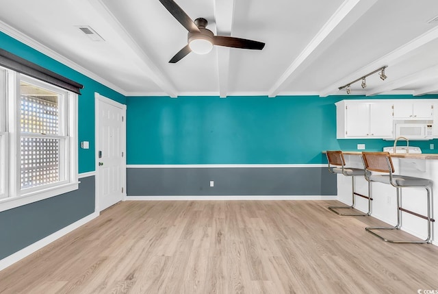 interior space with rail lighting, ceiling fan, crown molding, beam ceiling, and light wood-type flooring