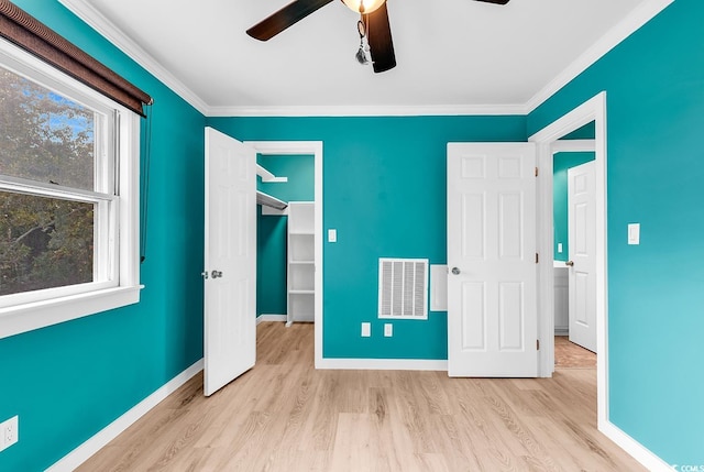 unfurnished bedroom featuring a closet, a spacious closet, crown molding, light wood-type flooring, and ceiling fan