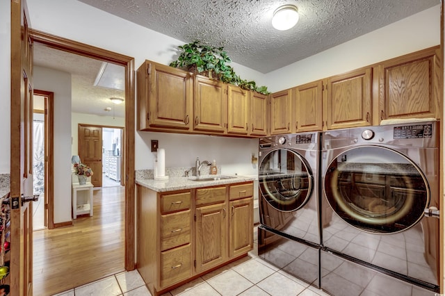 washroom with cabinets, a textured ceiling, sink, light hardwood / wood-style flooring, and independent washer and dryer