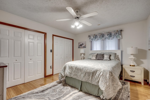 bedroom featuring a textured ceiling, light wood-type flooring, ceiling fan, and two closets