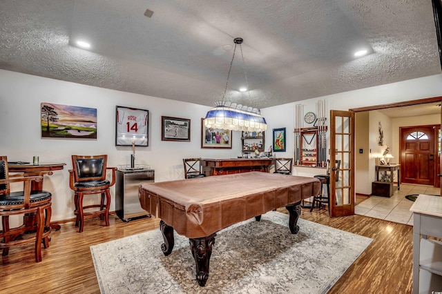 rec room with bar area, french doors, light hardwood / wood-style floors, and a textured ceiling