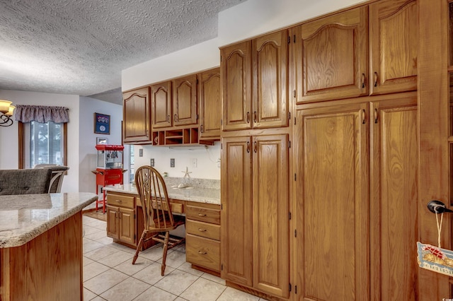 kitchen with light stone countertops, a textured ceiling, built in desk, and light tile patterned floors