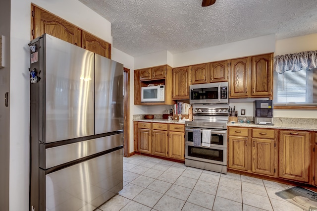 kitchen featuring a textured ceiling, stainless steel appliances, light tile patterned floors, and light stone countertops