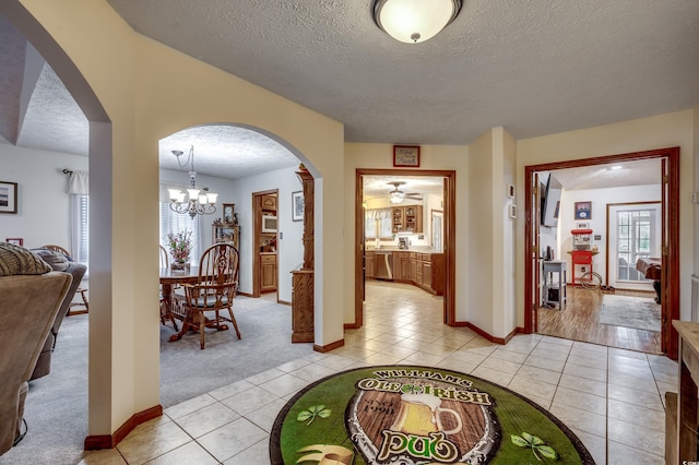 interior space with a textured ceiling, light tile patterned floors, and ceiling fan with notable chandelier