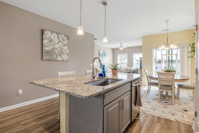 kitchen with sink, gray cabinetry, light stone countertops, a center island with sink, and stainless steel dishwasher