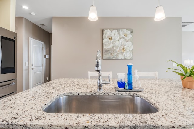 kitchen with light stone countertops, sink, refrigerator, and decorative light fixtures