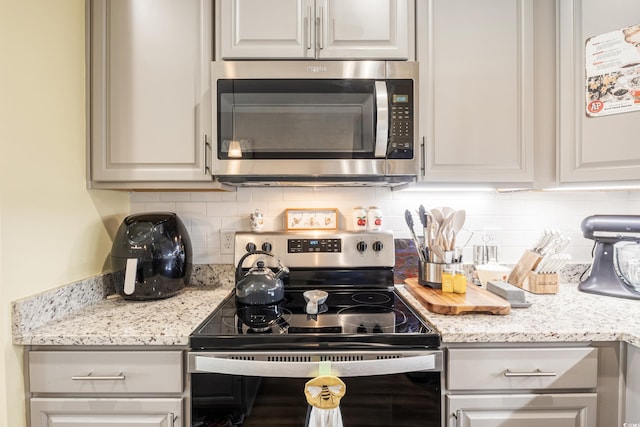 kitchen with stainless steel appliances, light stone countertops, and decorative backsplash