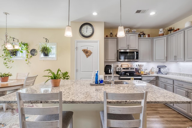 kitchen with pendant lighting, appliances with stainless steel finishes, a kitchen island with sink, and tasteful backsplash