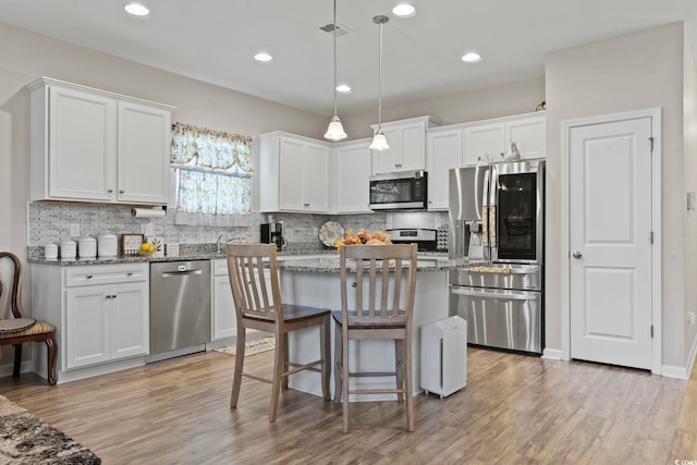 kitchen with light stone counters, pendant lighting, a kitchen bar, white cabinets, and appliances with stainless steel finishes