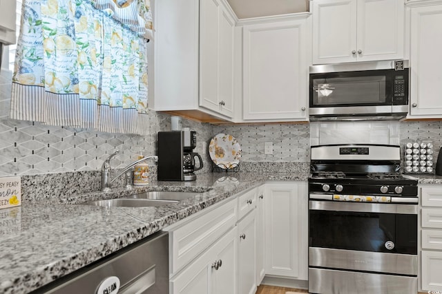 kitchen featuring light stone countertops, sink, backsplash, white cabinets, and appliances with stainless steel finishes