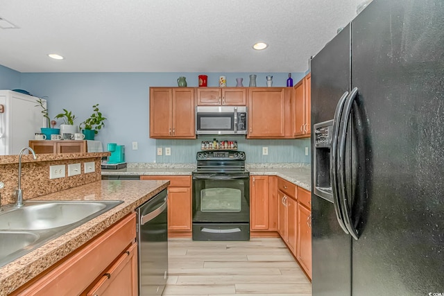 kitchen with sink, a textured ceiling, black appliances, and light hardwood / wood-style flooring