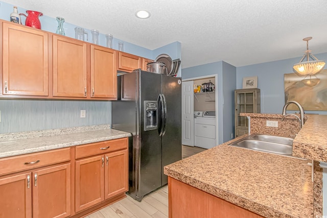 kitchen featuring black fridge, washer and dryer, a textured ceiling, light hardwood / wood-style flooring, and sink