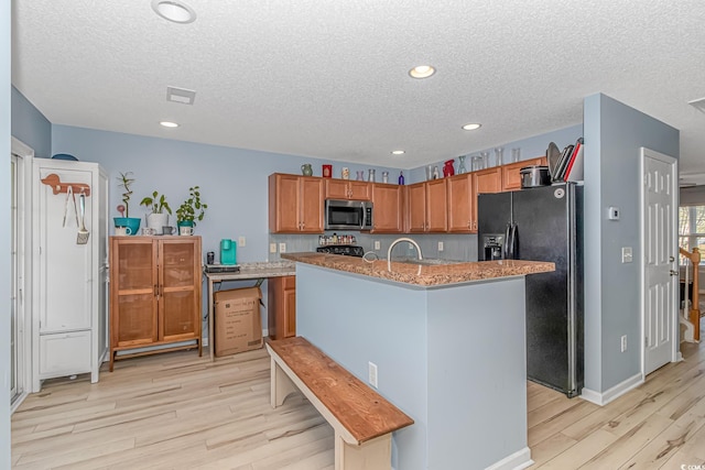 kitchen featuring light hardwood / wood-style flooring, a center island with sink, black appliances, light stone countertops, and a textured ceiling