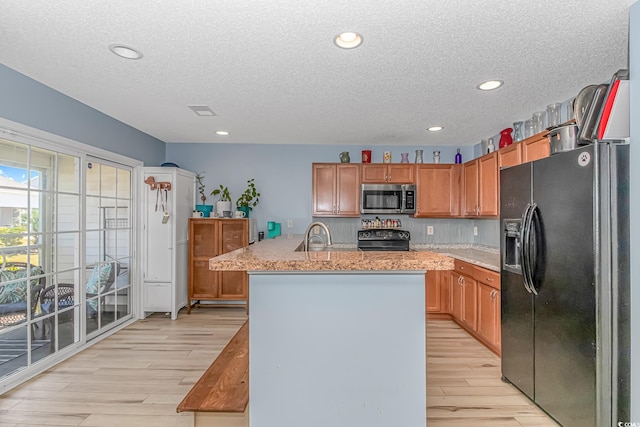 kitchen with a center island with sink, black appliances, light hardwood / wood-style flooring, and a textured ceiling