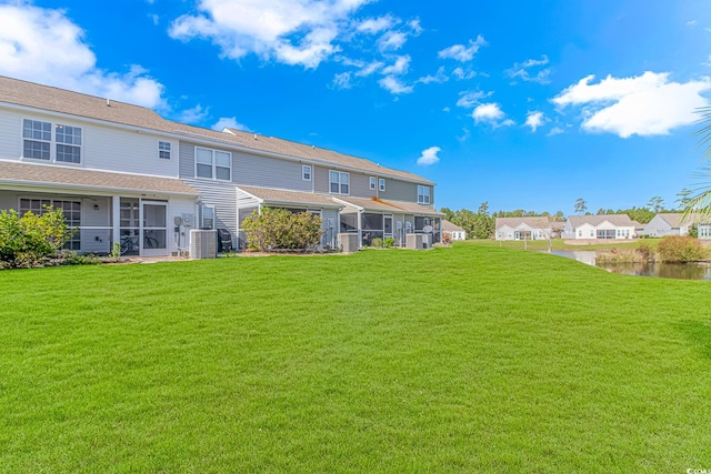 rear view of house featuring central air condition unit, a yard, and a water view