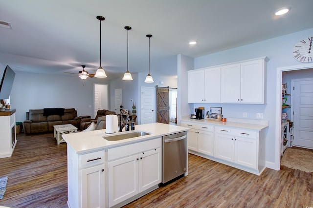 kitchen with white cabinetry, sink, a barn door, stainless steel dishwasher, and a kitchen island with sink