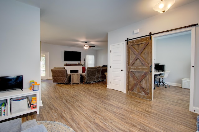 living room featuring ceiling fan, a barn door, and wood-type flooring