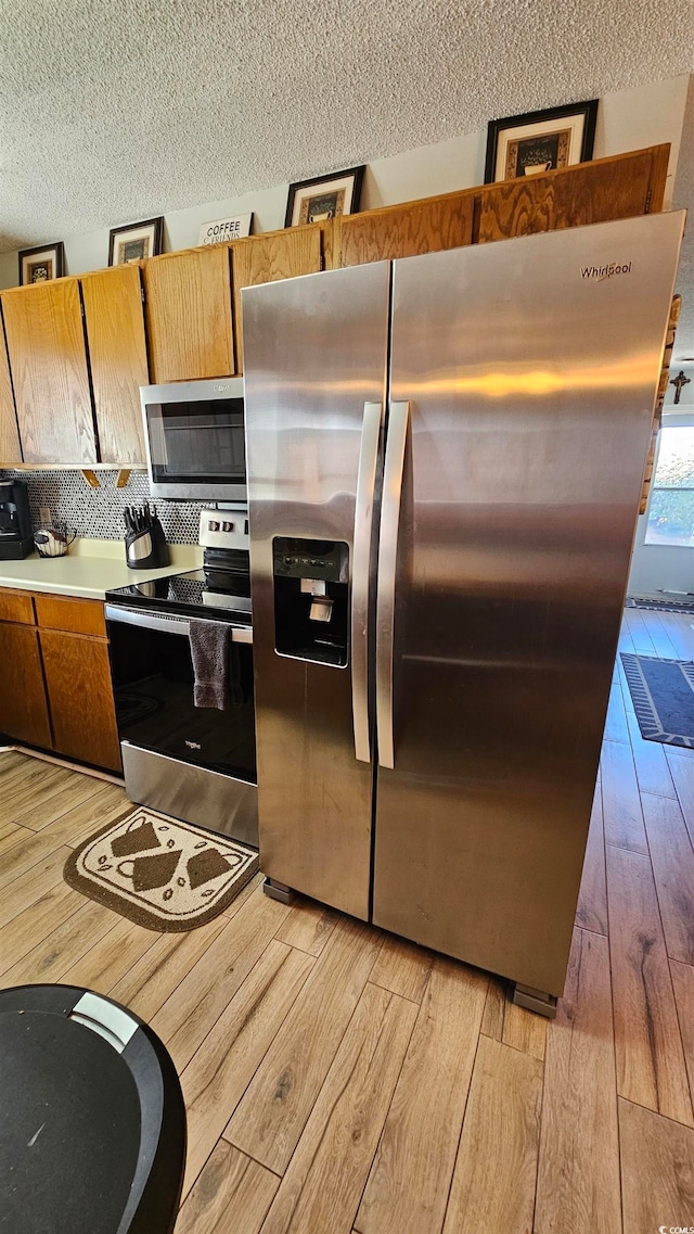 kitchen with backsplash, appliances with stainless steel finishes, a textured ceiling, and light hardwood / wood-style floors