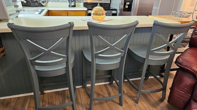 bar featuring wood-type flooring, black range oven, sink, and stainless steel refrigerator